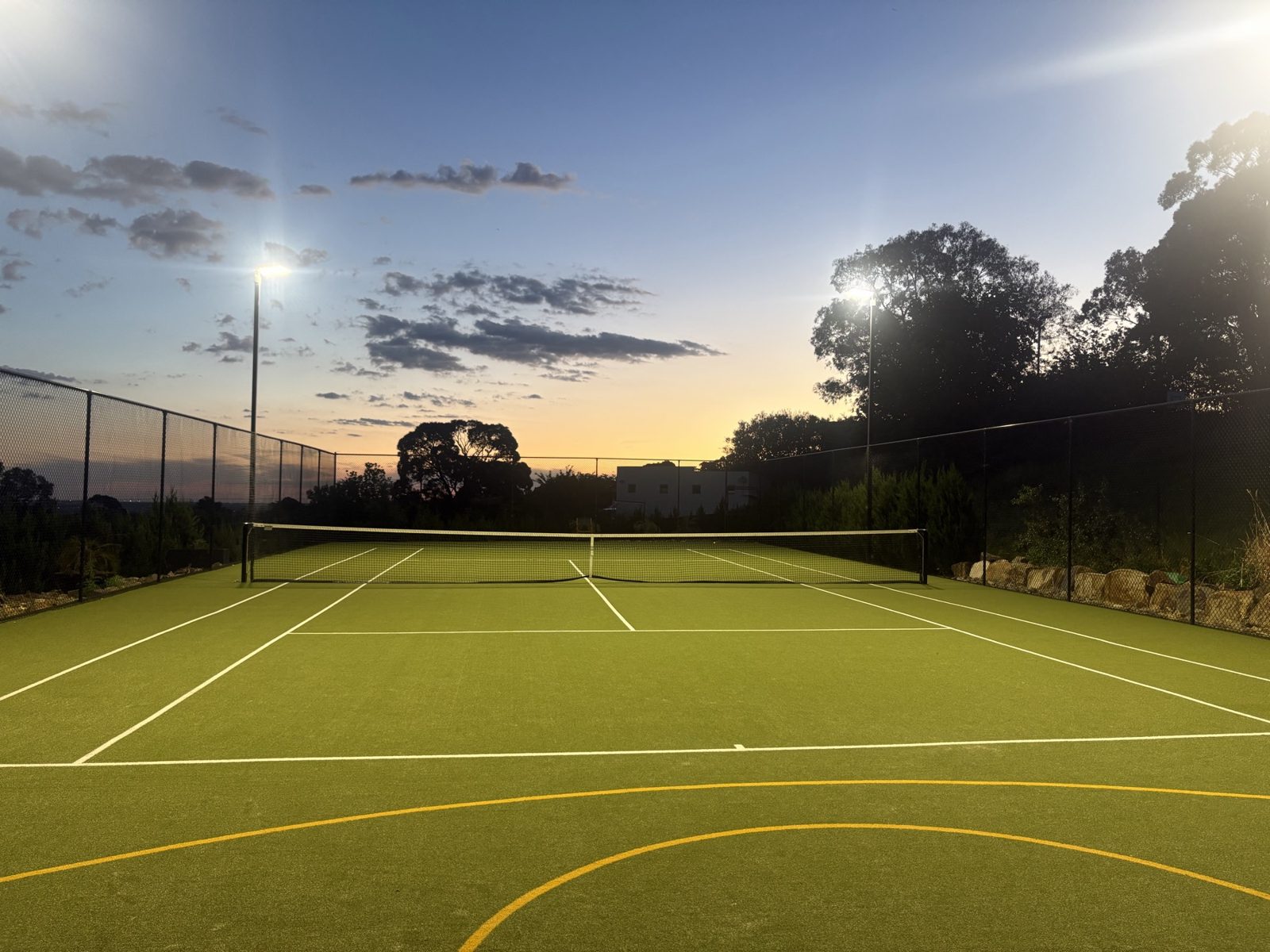 The tennis court at dusk with the floodlights on